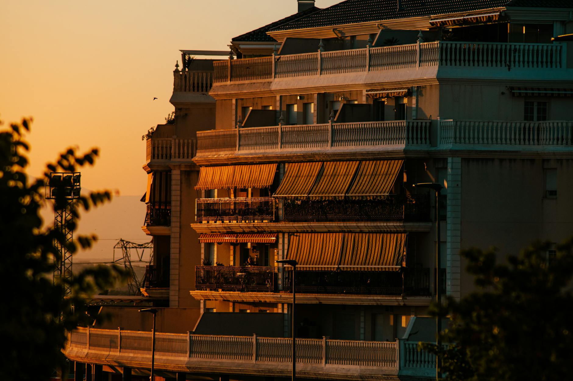 Sunset view of a modern urban apartment building with terraces and awnings, bathed in warm golden light.