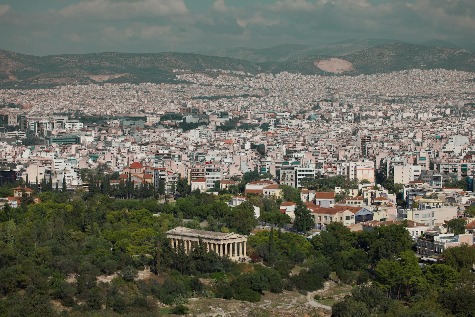 Panoramic view of Athens cityscape with ancient temple and greenery.