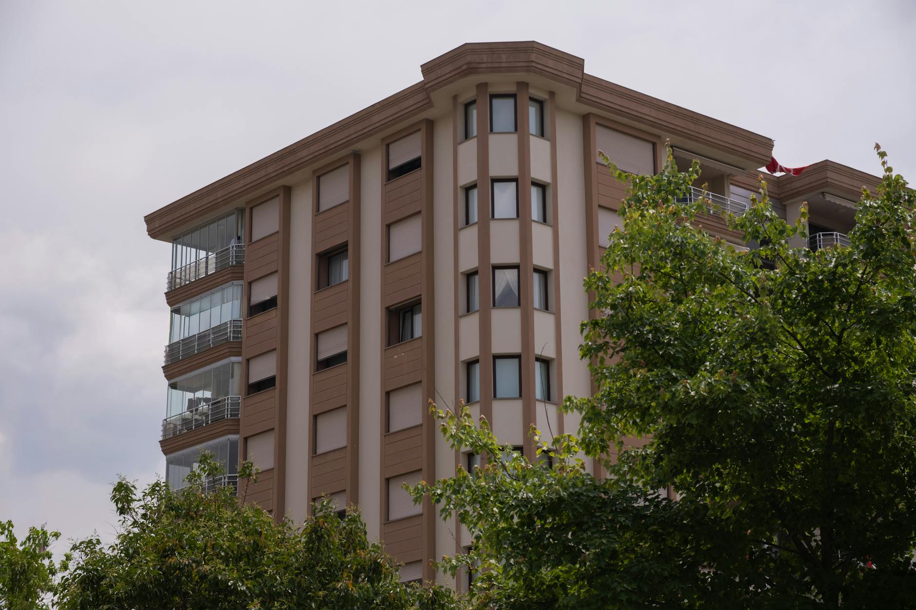A modern apartment building with glass balconies in İzmir, framed by greenery on an overcast day.