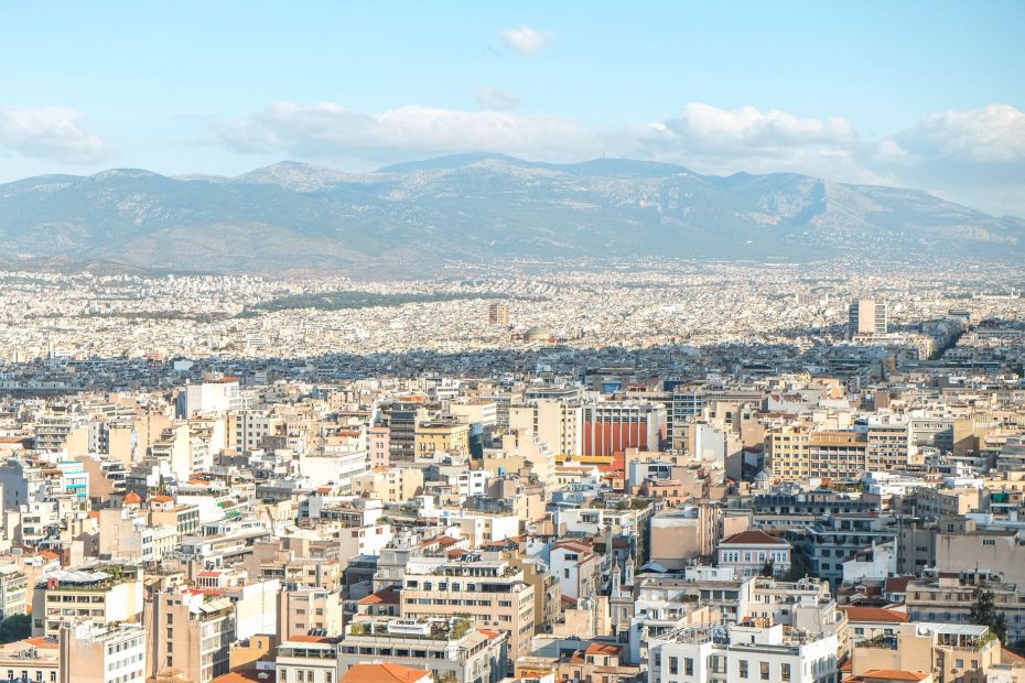 A breathtaking aerial view of Athens, Greece featuring urban sprawl and distant mountains under clear skies.